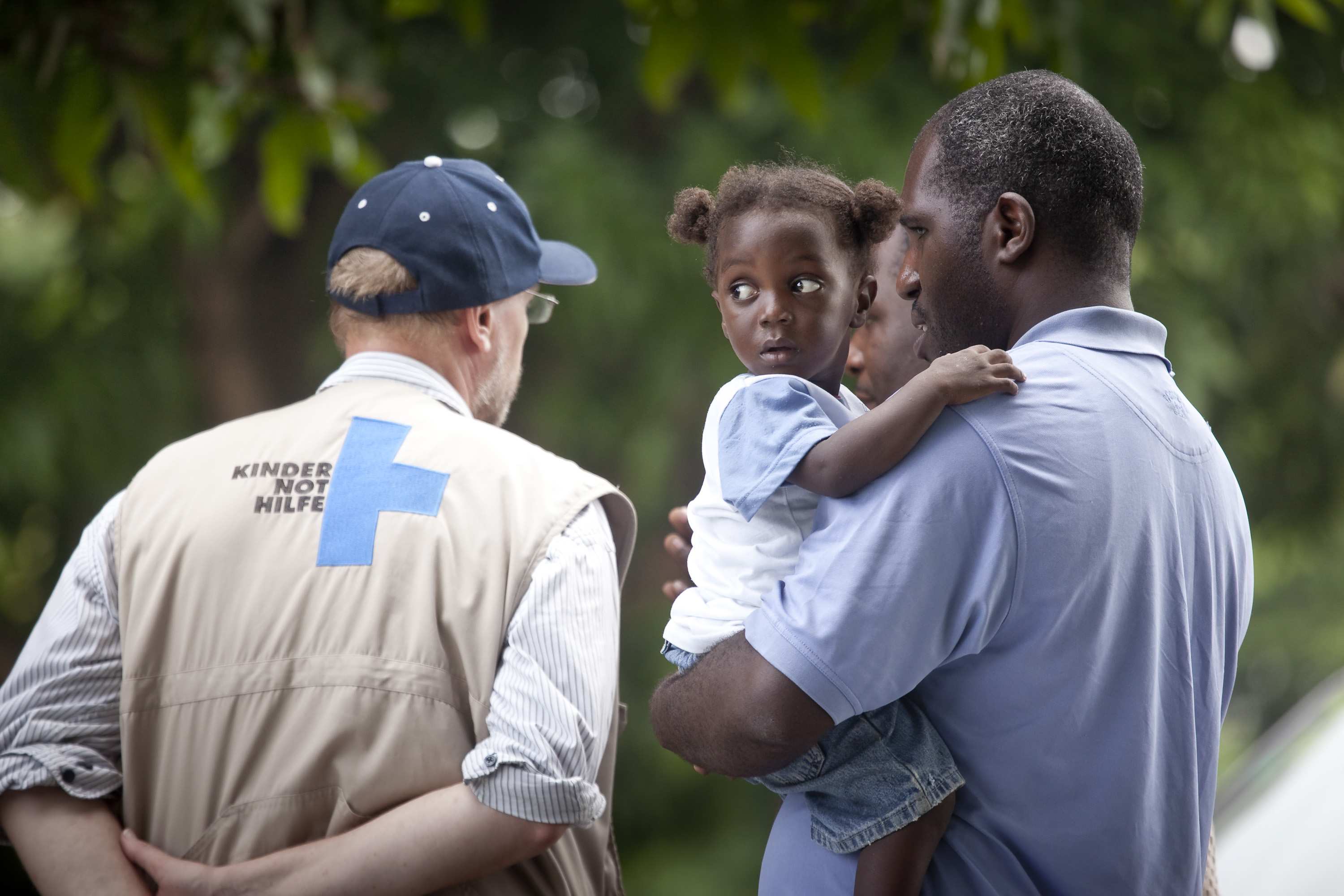 Mann hält kleines Mädchen im Arm, daneben nein Mann mit Logo der Kindernothilfe auf der Weste (Quelle: Jakob Studnar)