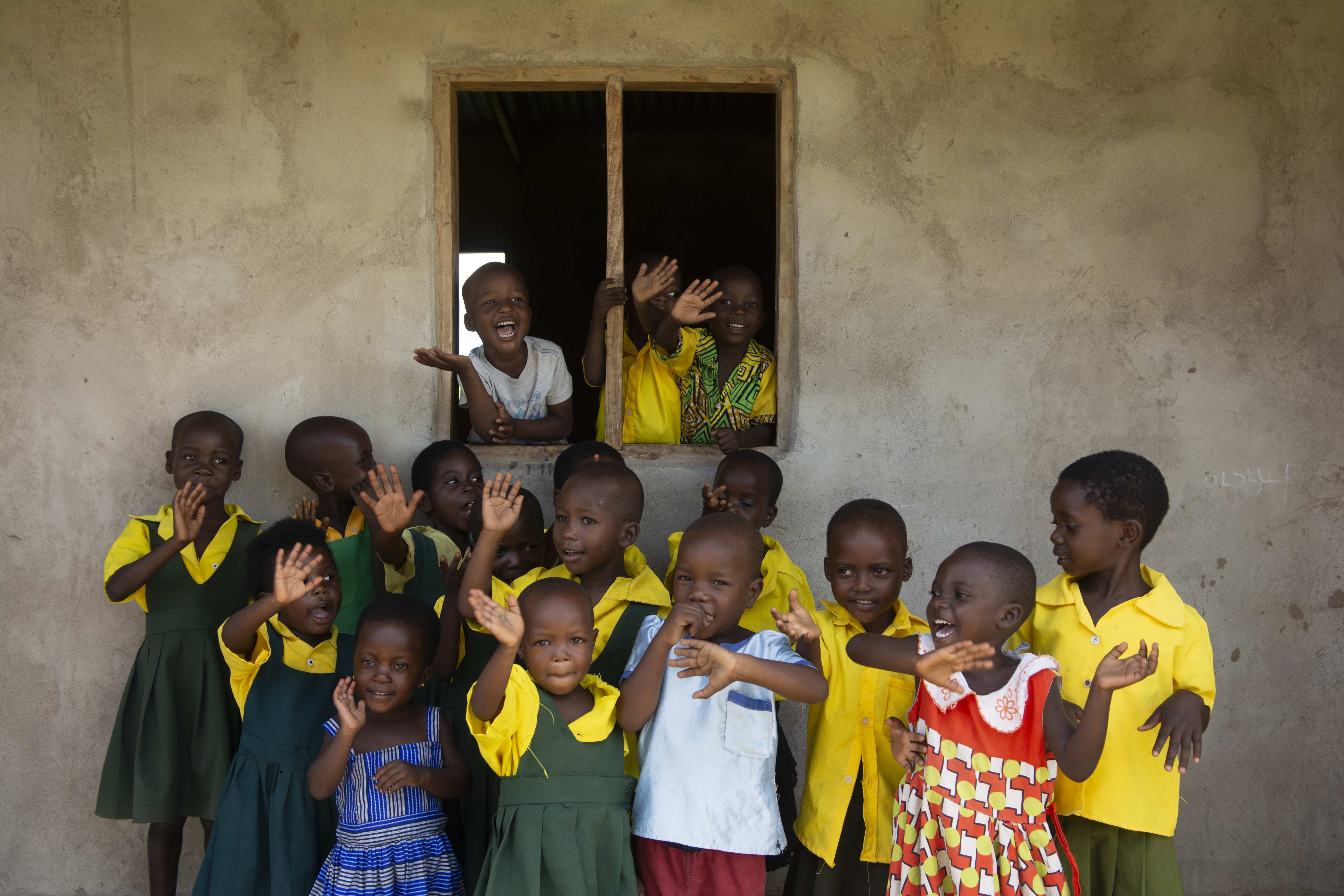 Children in school uniform wave in front of and out of a window of a preschool (source: christian nusch)