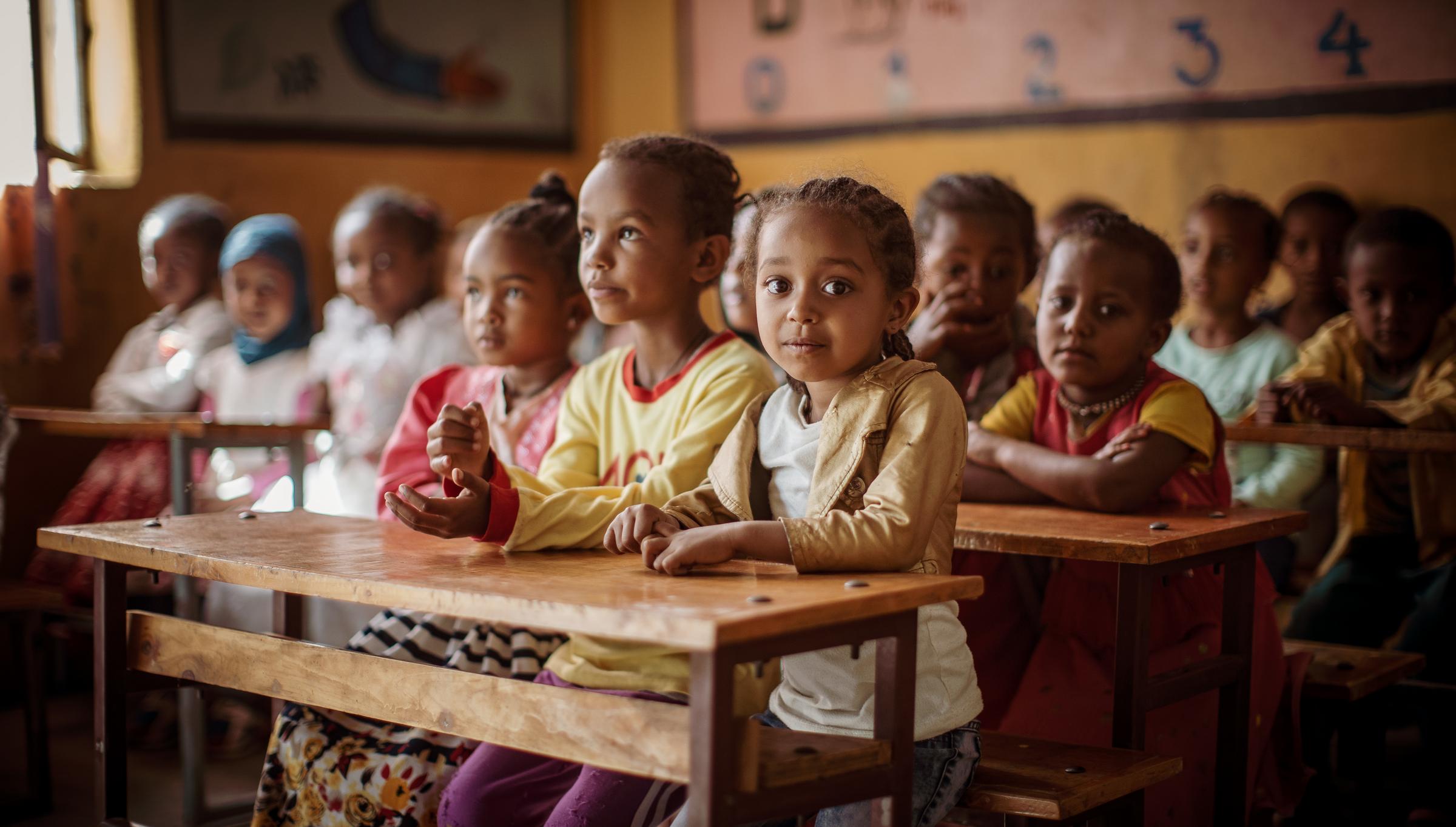 A girl sits with several children in a class room in Ethiopia and looks towards the camera (source: Jakob Studnar)