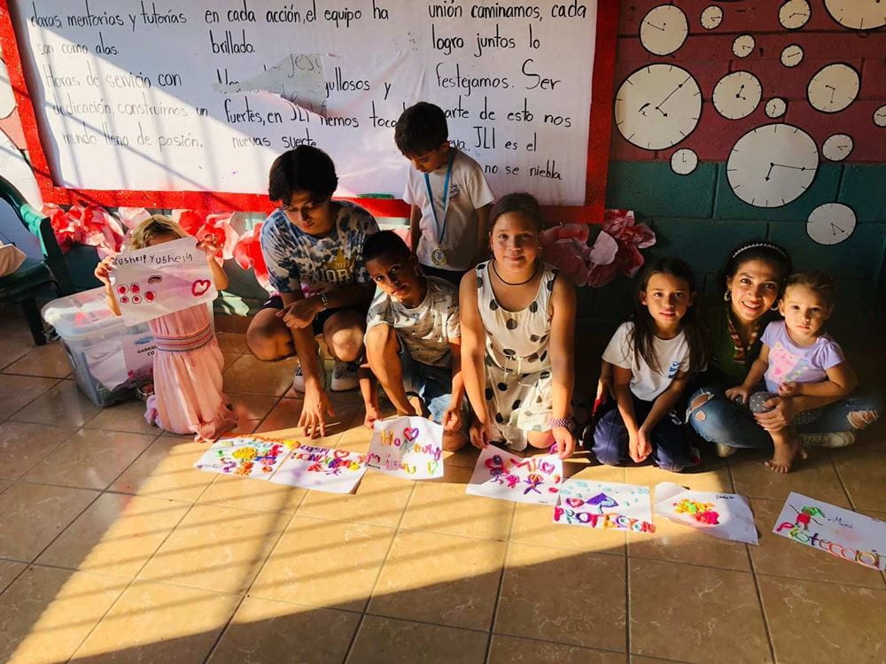 Los niñas y niños del proyecto se sientan frente a una pizarra y presentan carteles diseñados por ellos mismos (fuente: ASJ Honduras/CASM Honduras).