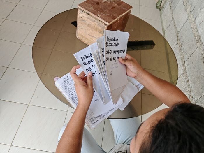 A woman holds individual record books of a self-help group in her hands (Source: Kindernothilfe-Partner)